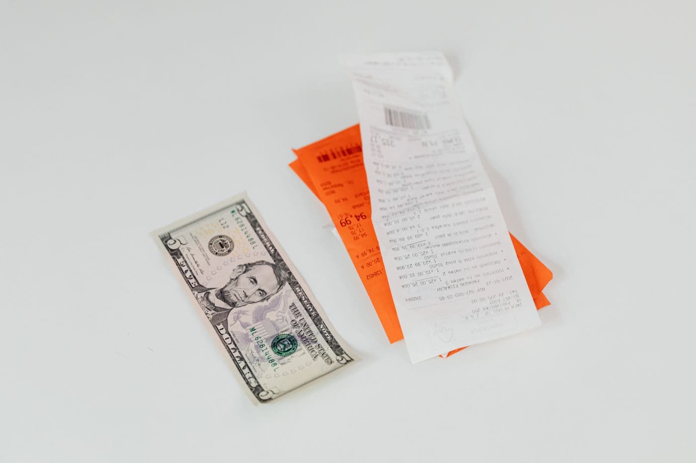 A few shop receipts and a five dollar note on a pale surface.